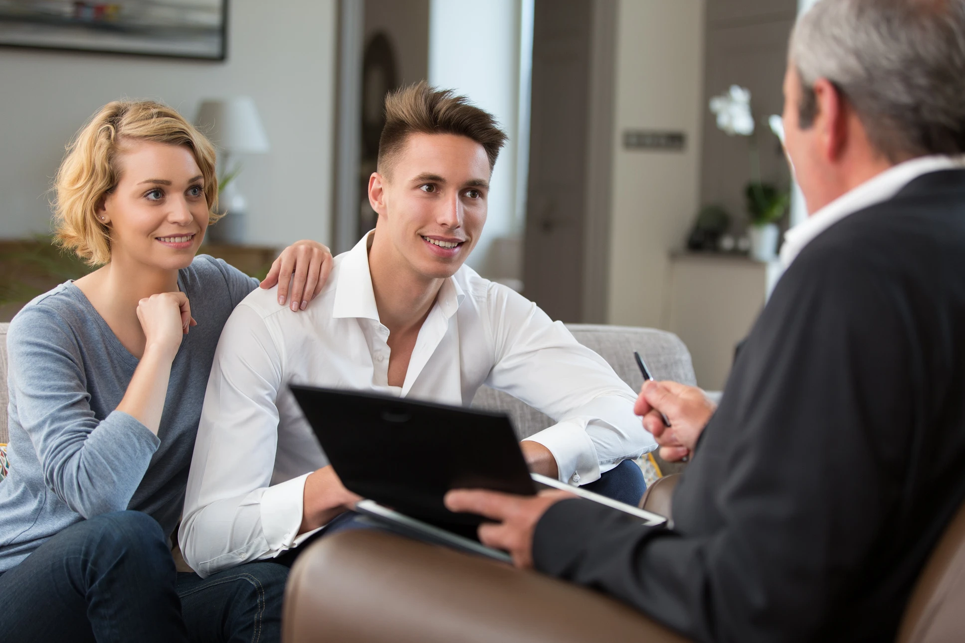 Scène de consultation professionnelle en intérieur moderne avec couple assis sur canapé gris face à conseiller en costume