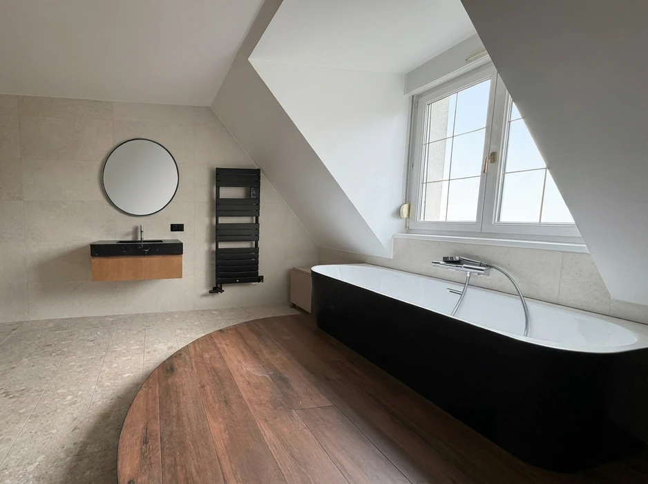 Salle de bain mansardée haut de gamme avec baignoire îlot noir et blanc sur plateforme en parquet bois