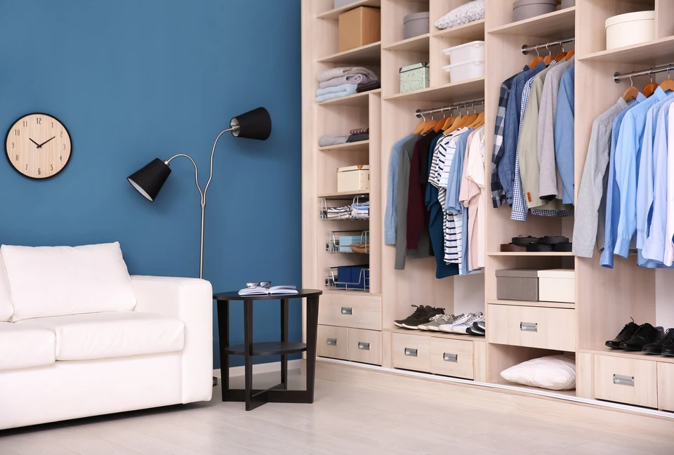 Intérieur élégant d'un showroom privatif de luxe dédié à l'agencement intérieur. La scène montre un espace lumineux et aéré, avec des murs neutres ou clairs, présentant des configurations réelles de dressings, placards et rangements sur mesure. Au premier plan, on distingue des matériaux d'exception (carrelage premium, échantillons de revêtements de sol PVC et stratifié) exposés sur des présentoirs ou tables de consultation. L'atmosphère est calme, épurée et valorisante, loin de l'ambiance de magasin grand public. Aucun client n'est visible, ou éventuellement un professionnel seul examinant les matériaux. L'éclairage est professionnel et flatteur, mettant en valeur la qualité des finitions et des détails.