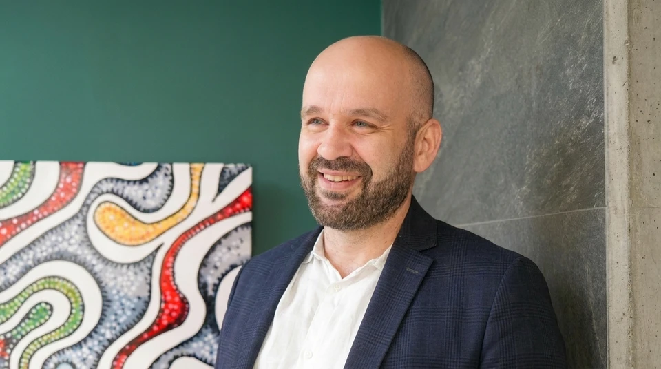 Un professionnel en agencement int&eacute;rieur (apparence soign&eacute;e, v&ecirc;tu professionnellement) pr&eacute;sent&eacute; dans un showroom moderne et lumineux, en train de discuter avec un client devant des plans ou des &eacute;chantillons de mat&eacute;riaux (carrelage, rev&ecirc;tements). L'interaction montre une &eacute;coute active et un accompagnement personnalis&eacute;. La sc&egrave;ne capture le moment de la relation client premium et du conseil en conception, illustrant la continuit&eacute; et la coh&eacute;rence du suivi. Arri&egrave;re-plan professionnel montrant des &eacute;l&eacute;ments d'agencement (cuisine design, rangements sur mesure, salles de bain).